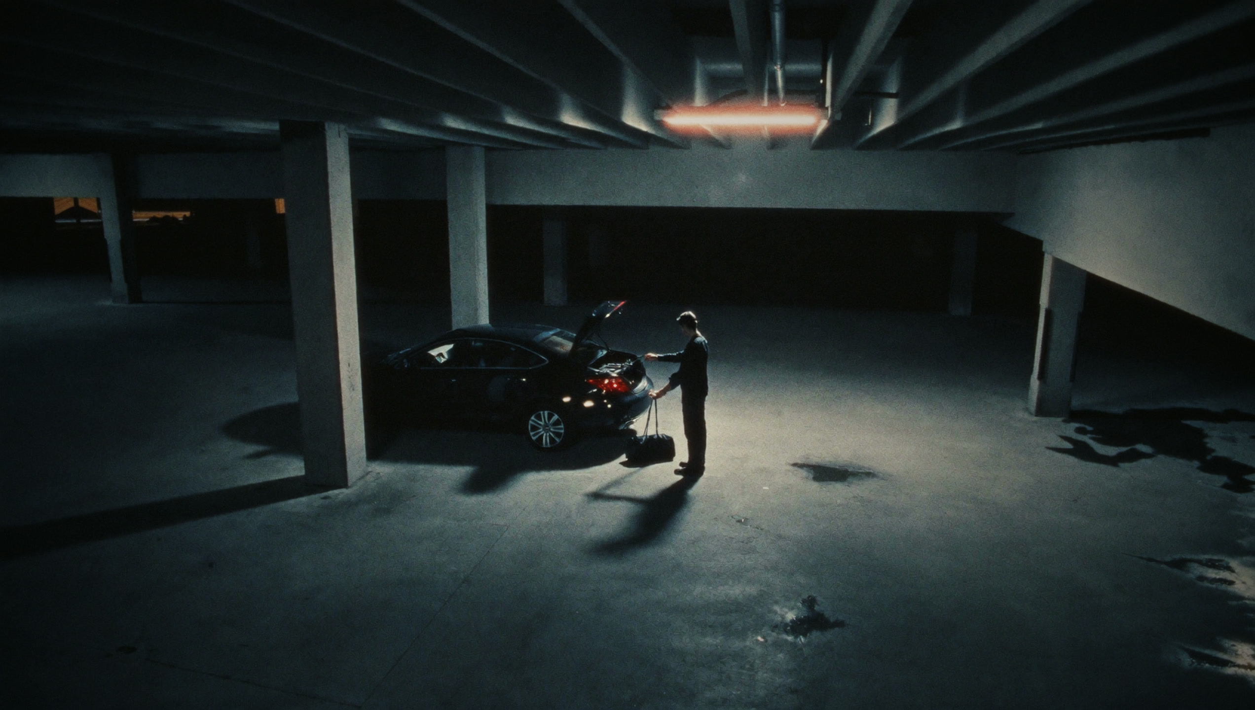 Loading a black duffel into a car in a dark garage