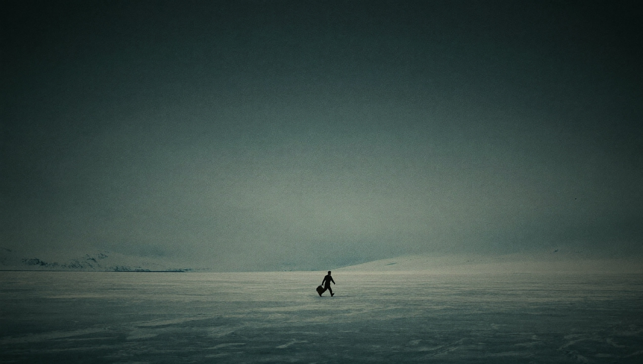 A man crossing a frozen lake with a black duffel