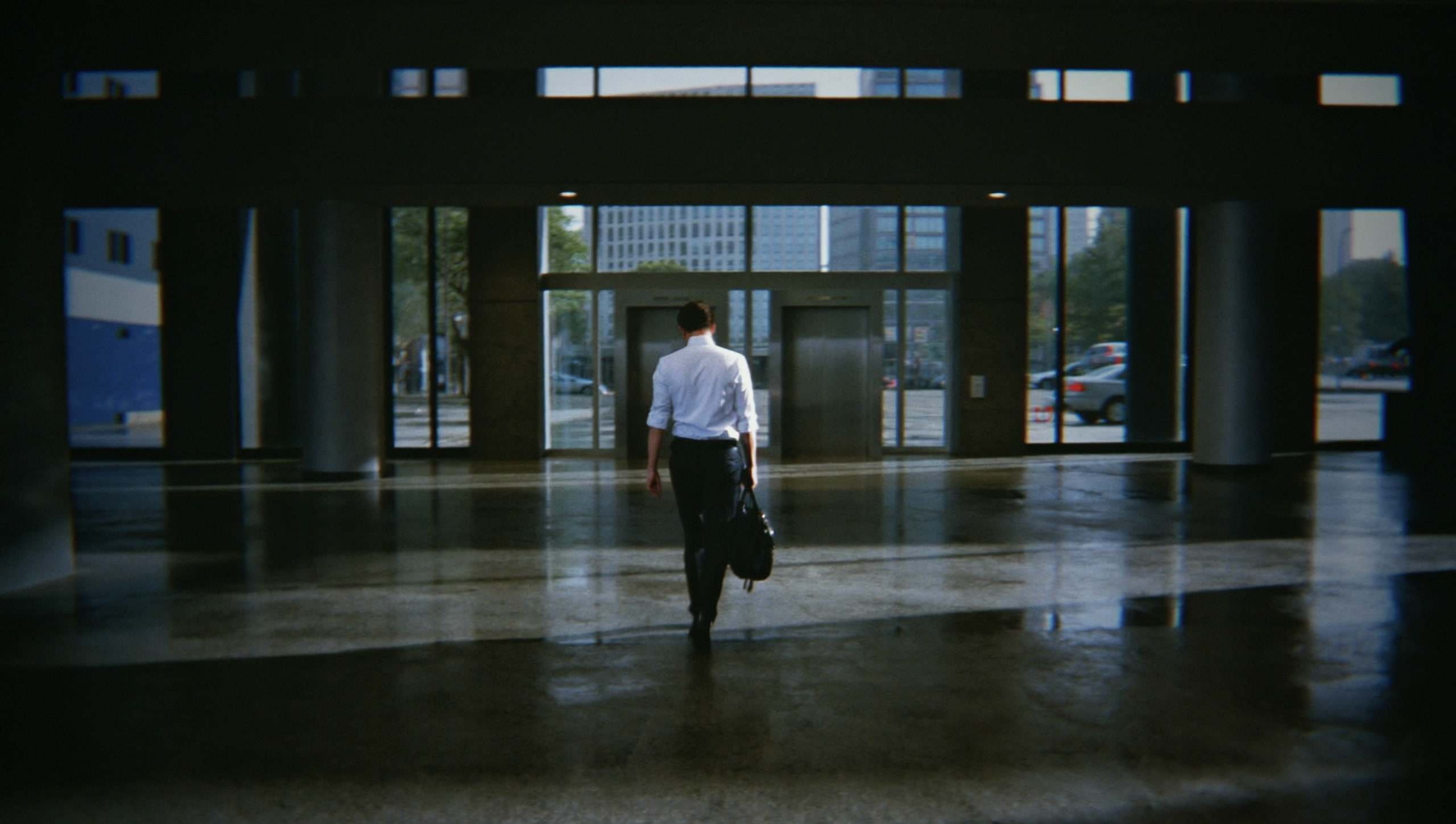 A man in a white shirt crossing an empty office lobby with a black duffel